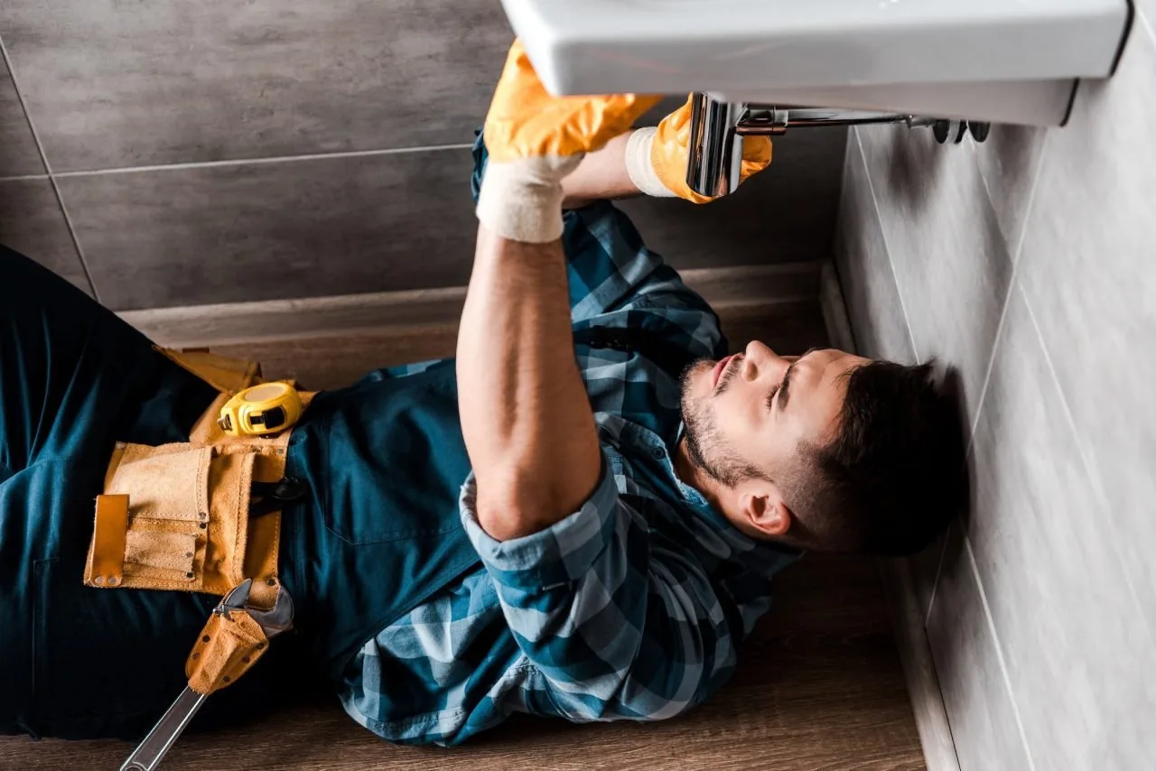 Plumber inspecting water damage beneath a bathroom sink