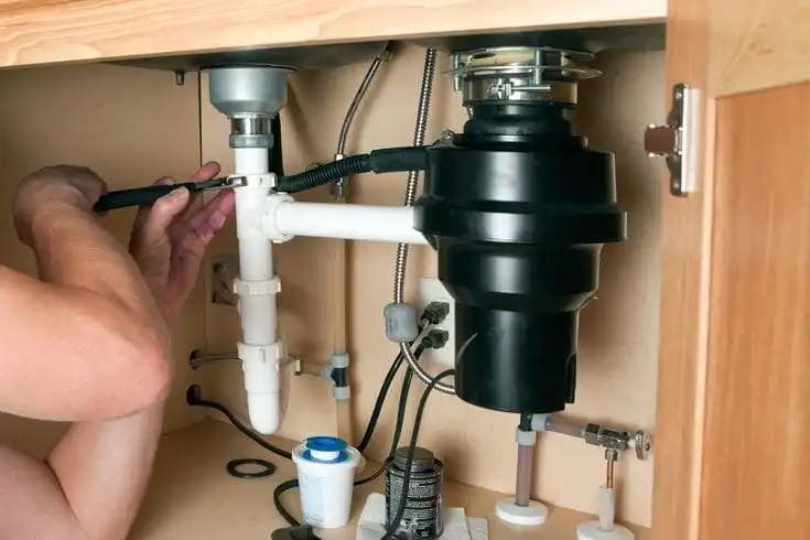 Plumber repairing a garbage disposal beneath a kitchen sink