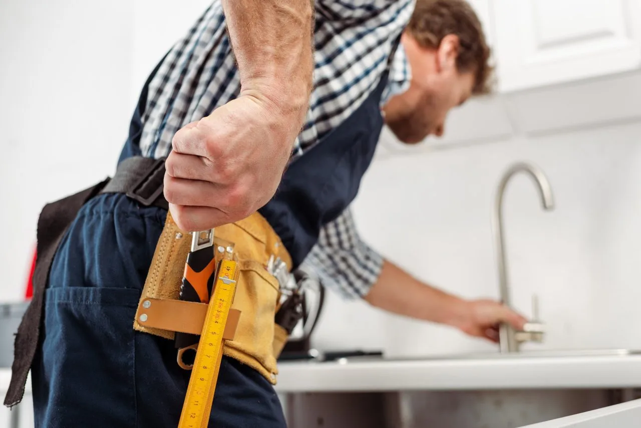 Plumber reaching for a wrench while repairing a kitchen faucet