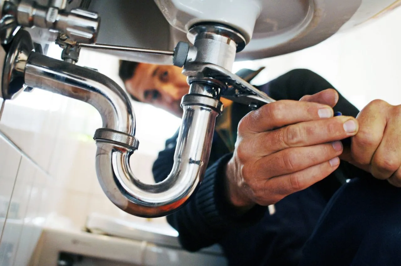 Plumber tightening a drainpipe beneath a bathroom sink