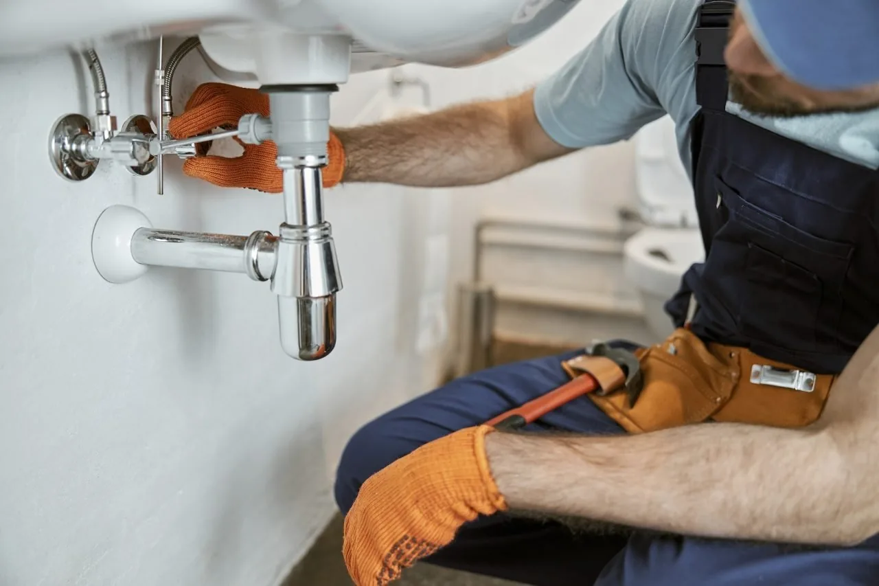 Plumber repairing pipes beneath a bathroom sink